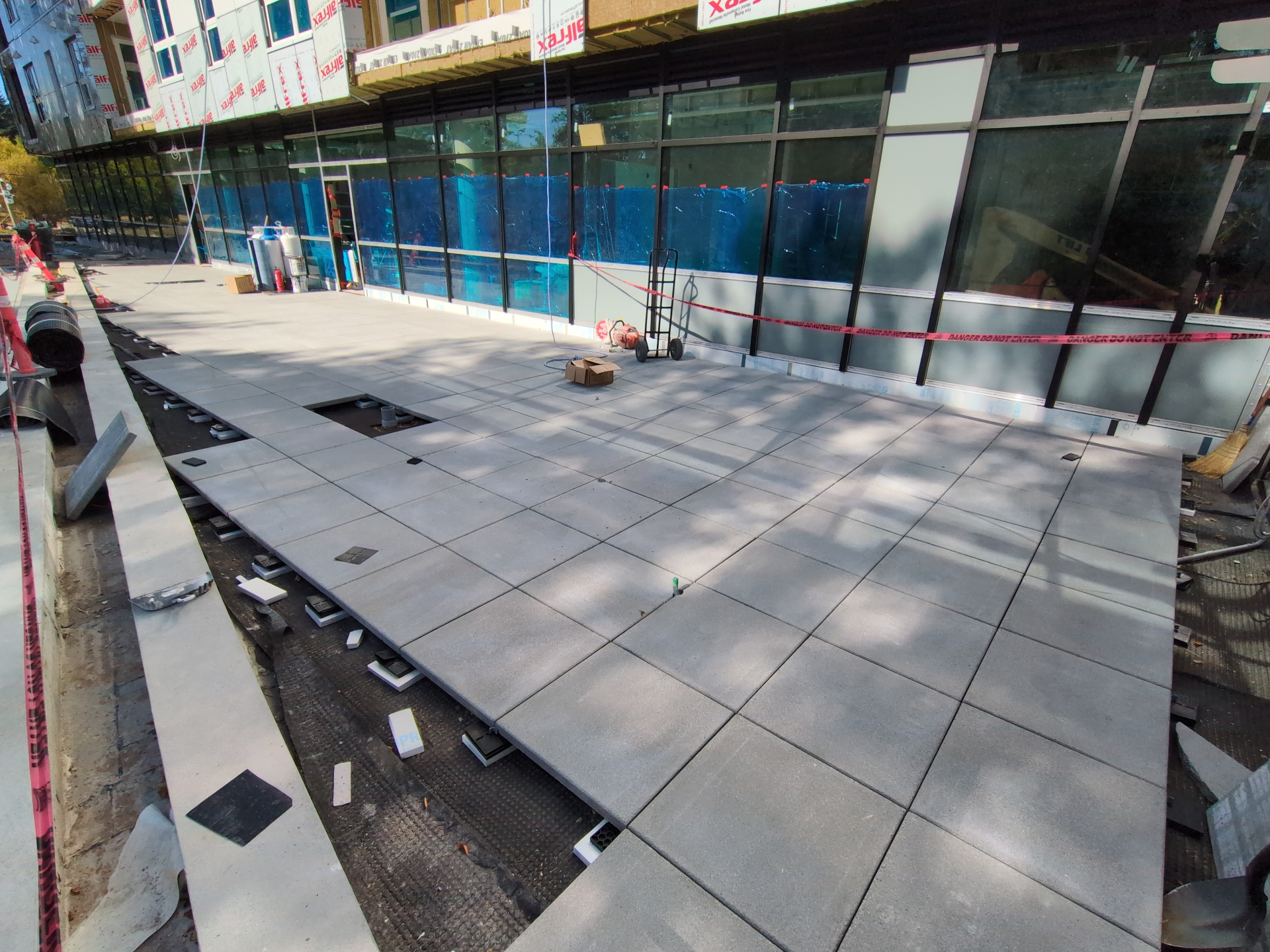 Pedestal-set granite pavers being laid across the courtyard outside the storefront