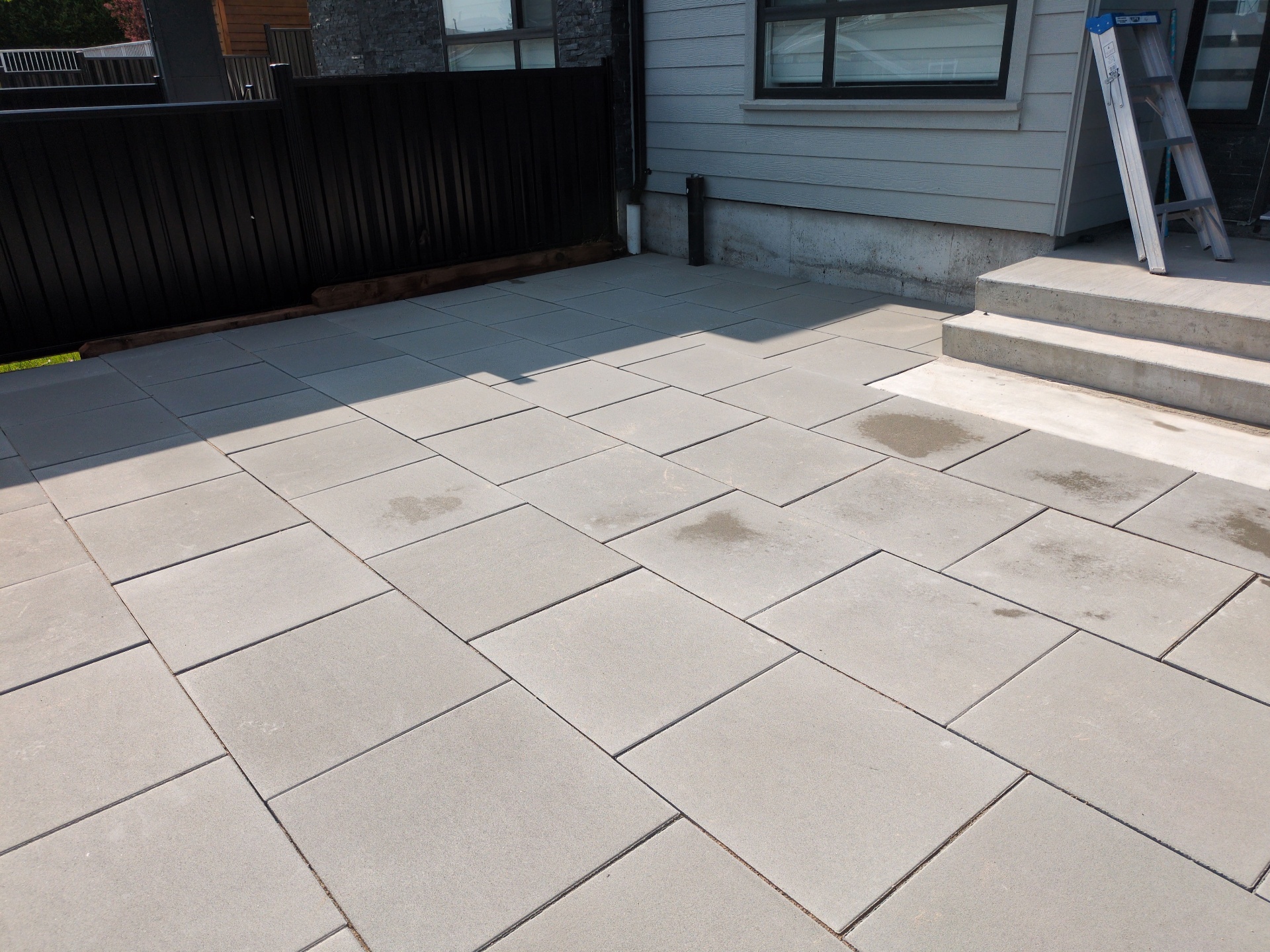 Mid-install slab pavers being set in a running pattern beside the home's concrete steps