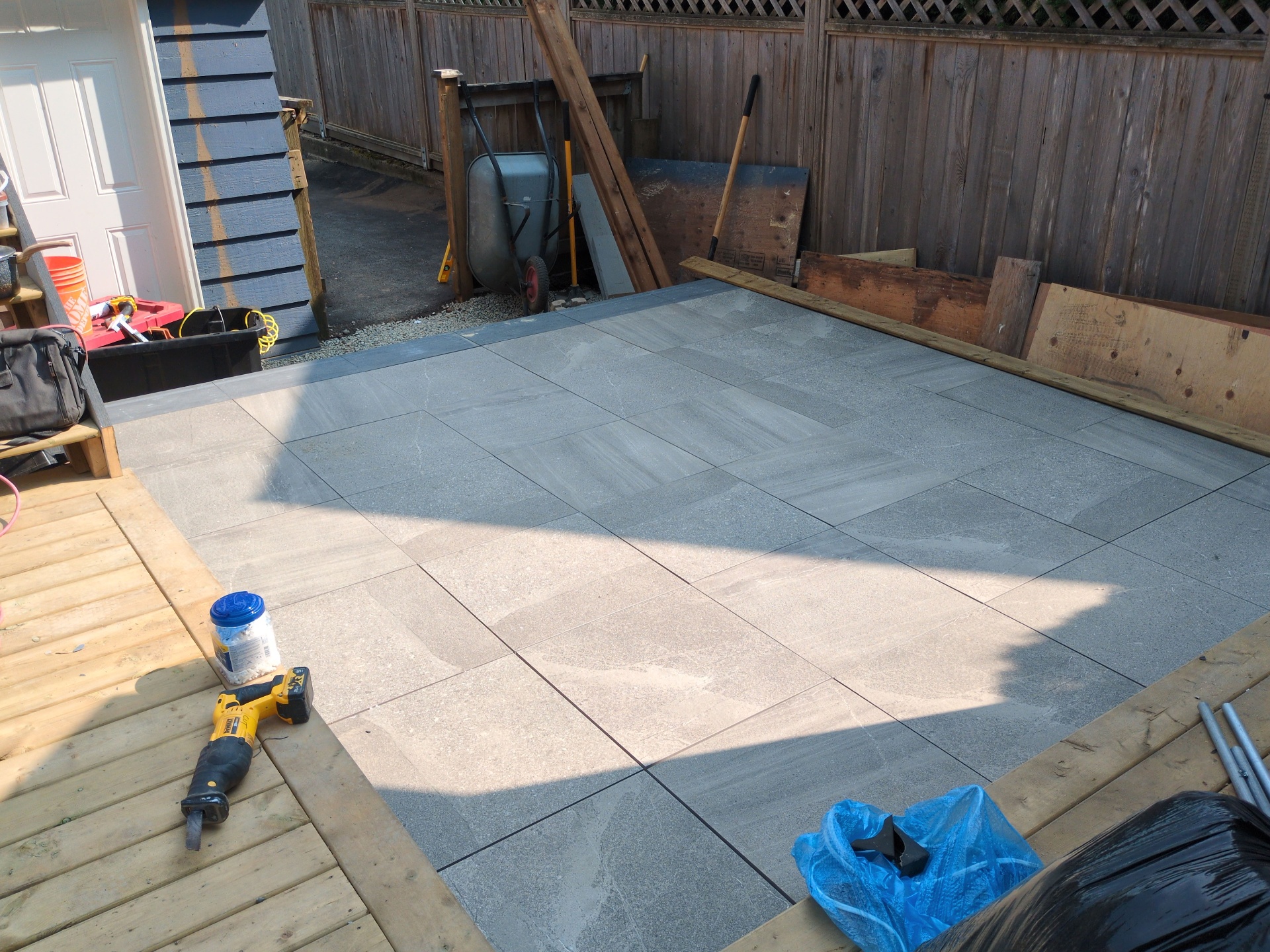 Grey slab pavers being laid in a running pattern between the deck and back fence