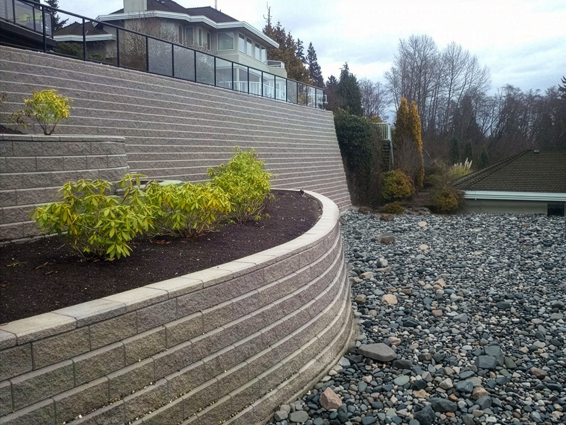 Curved tier sweeping right across the slope with planted bed and lower river-rock drainage