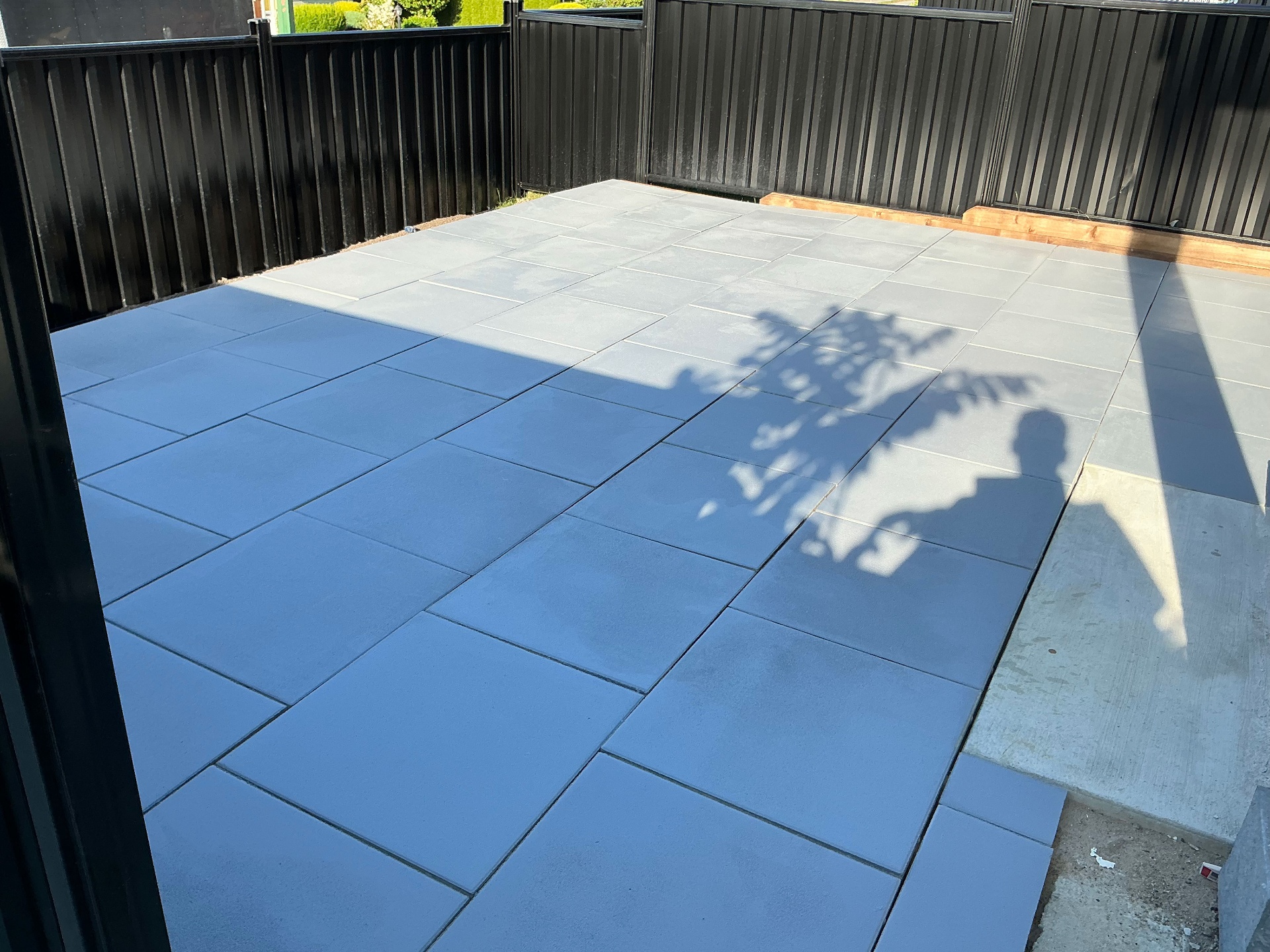 Wide finished slab patio under afternoon shadow with black metal fence behind